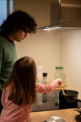 Young father and little child girl, profile view, cooking together in modern white kitchen. Vertical shot.