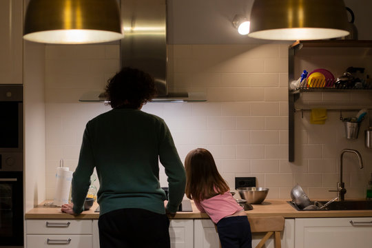 Young father and little child girl, back view, cooking together in modern white kitchen with big brass lamps