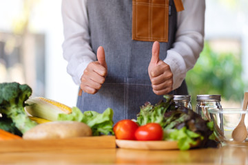 Closeup image of a female chef making and showing thumbs up hand sign while preparing fresh mixed vegetables to cook in kitchen