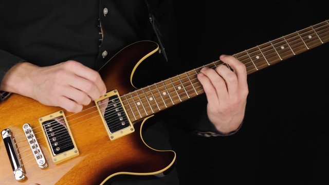 Guitarist plays a light brown six-string electric guitar with a pick against black background. Concept of stay at home and make some music. Free time for sound art. Wide shot. 4K