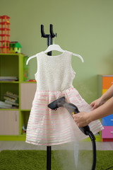 Woman ironing the kid dress with a steam generator in the children room