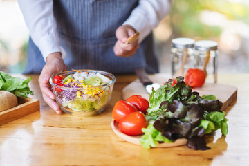 Closeup image of a female chef cooking and holding a bowl of fresh mixed vegetables salad in kitchen