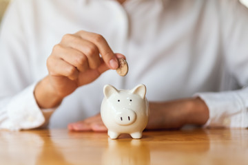 Obraz na płótnie Canvas A woman putting coins into piggy bank for saving money concept