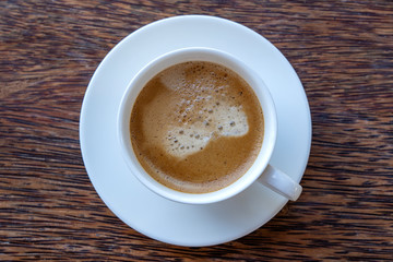 White cup of fresh coffee on wooden table, top view