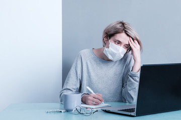 Young sad woman in a mask at a computer makes notes looking for information on the Internet. Pandemic Corona Virus covid 19. empty spase fo text