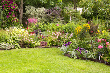 Beautiful colorful flower garden with blooming flower beds and a green lawn in summer - obrazy, fototapety, plakaty