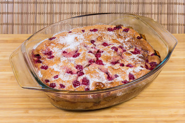 Cherry clafoutis in glass casserole pan on the wooden surface