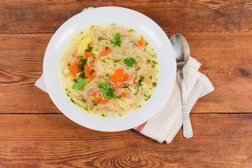 Chicken vermicelli soup in dish, spoon on napkin, top view