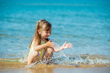 Little 3 year old girl in a bathing suit sits on the sandy seashore and plays with the sea,...