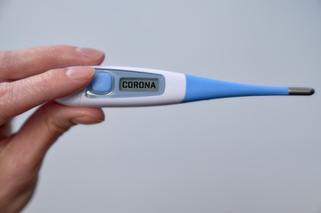 Male hand holds clinical thermometer with corona text on the screen during global covid-19 or corona pandemic.