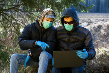 Boy and man in protective sterile medical mask on faces looking at laptop in forest