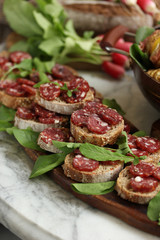 Summer snacks. Bread with sausage and herbs on a wooden board. A bunch of radishes, a pan with potatoes on a light table. Background image, copy space