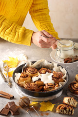 The concept of American cuisine. Pastries and desserts. Cinnabon and white glaze with hands. Buns with cinnamon and cream cheese on a light background. Background image, copy space
