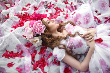 A tender portrait of a beautiful girl in a bright wreath of peonies lying among the petals.