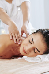 Smiling pretty young woman enjoying shoulder massage in spa salon