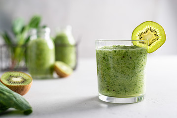 Freshly blended green fruit smoothie in a glass on light background with ingredients. Close up,...