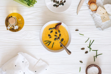 Pumpkin cream soup with cheese and onions on a white board. Still life flat lay