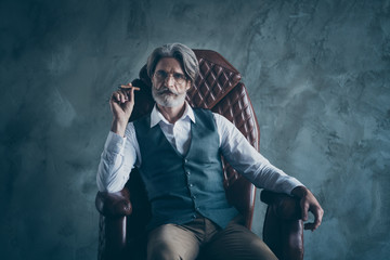 Portrait of charismatic elegant old man boss company owner sit chair hold cigar wear white shirt brown pants trousers isolated over grey color background