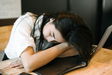 Young attractive Asian business woman sleeping, drowsing or taking a nap at her desk, Tired business woman accountant with bills and paper folders in office, tired young business woman with laptop.