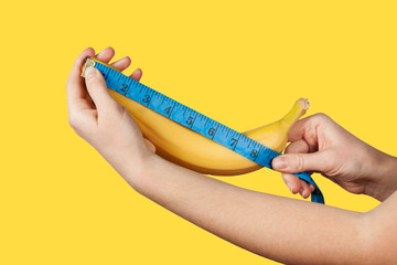 Measuring the size of a banana as a symbol of the male penis on yellow background. Big dick length. Strong erection and impotence problem. - obrazy, fototapety, plakaty