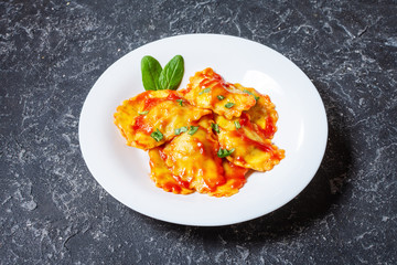 Ravioli with tomato sauce and basil on a dark stone background. Delicious pasta
