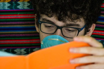 Portrait of a bedridden caucasian boy wearing a blue protective mask. He is studying his...
