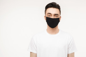Young man in white t-shirt and black protective mask isolated on white background. Healthy lifestyle concept, seasonal illness, and seasonal flu concept. Man wearing medical mask to prevent infection