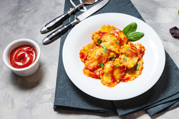 Ravioli with tomato sauce and basil on a concrete background. Delicious pasta