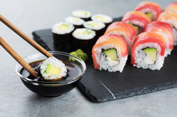 Sushi maki with avocado, sushi philadelphia, soy sauce and wasabi. Chopsticks taking portion of sushi roll. © vitals