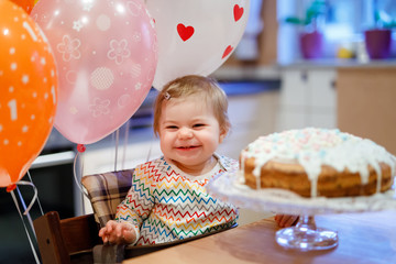 Adorable little baby girl celebrating first birthday. Baby eating marshmellows decoration on homemade cake, indoor. Birthday party for cute toddler child, beautiful daughter