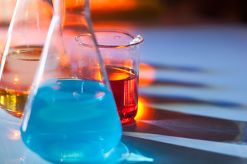 Illuminated laboratory flask filed with colorful chemical solutions with shadows on the table....