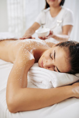 Beautician applying salt scrub on back of young woman