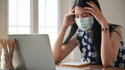 Girl wearing a mask and touching her head She works at home to protect against the Covid-19 virus.