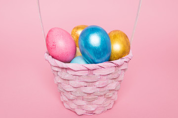 Multi-colored Easter eggs in a basket on a pink isolated background. Easter is a bright holiday.