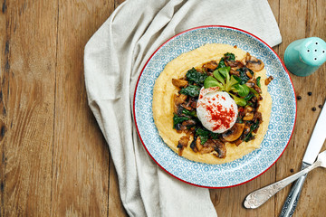 Corn porridge or polenta with fried mushrooms and poached egg in a blue ceramic plate on a wooden...