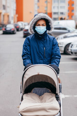 Young mother in surgical mask and gloves walking with baby outdoor in Europe