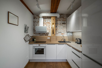 Contemporary loft interior of kitchen in apartment. Brick wall. Wooden surface. White kitchen set.