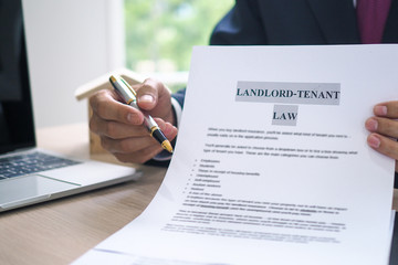 The hand of a man holding a house purchase contract with a pen showing up to customers. House salesman is showing Landlord-Tenant Law document.