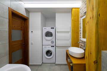 Modern loft interior of bathroom. Wooden design. Brick wall. White sink and mirror. Washing machine.