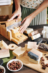 Woman cutting handmade fragrant soap into small bars with sharp knide in special mold - obrazy, fototapety, plakaty