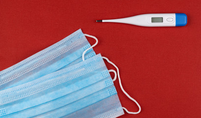 Surgical respiratory bandage face and electronic thermometeron on red background.