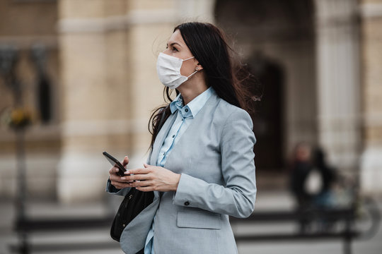 Young and elegant business woman standing on empty city street and wearing protective mask to protect herself from dangerous flu or virus. Corona virus or Covid-19 concept.