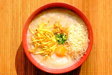 Delicious rice porridge (congee) for breakfast served in a bowl on bamboo plate mat.