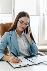 Businesswoman talking on mobile phone while writing sticky notes.