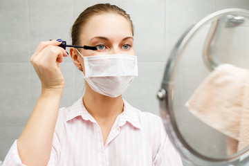 Close-up of young blonde in medical with mascara and mirror in hand