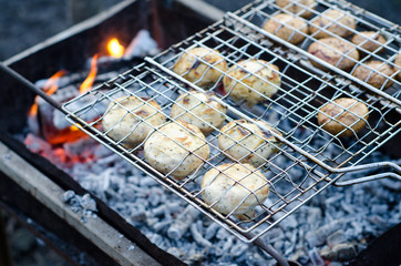 Delicious champignon mushrooms in soy sauce and mayonnaise are fried in grid on grill steam, on homemade grill, closeup