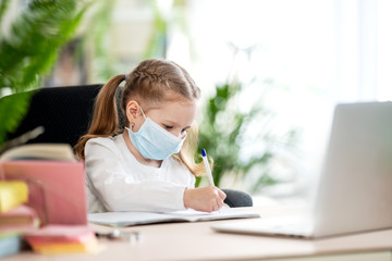 Cute little girl, doing homework, writing in notebook, using laptop, e-learning