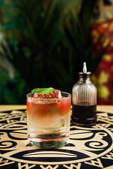 A tiki style colourful layered cocktail in a rocks glass with crystal clear ice cube, garnished...