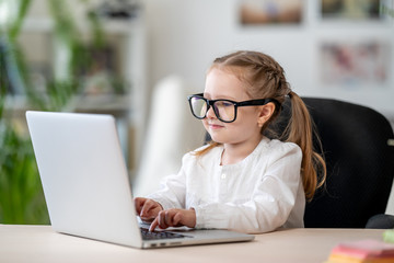Cute little girl wearing glasses using laptop digital e -learning concept
