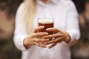 A blonde girl in a white shirt holds a glass of coffee in her both hands